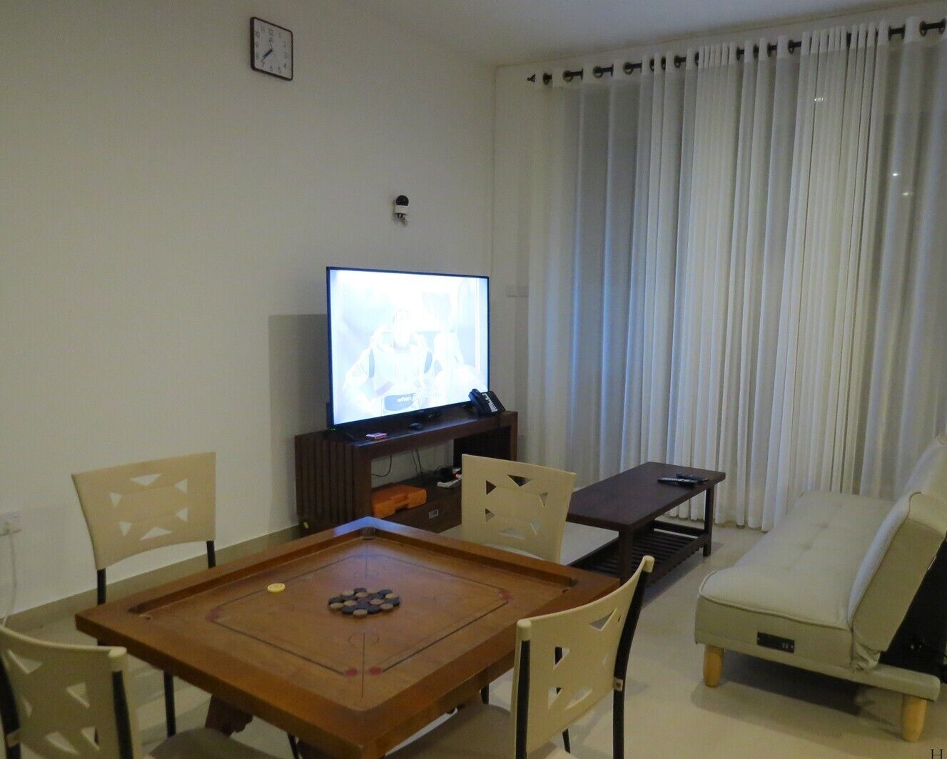 A living room with a television, a wooden table with a board game, a sofa, and a chair.