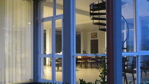 Een modern gebouw met grote glazen deuren die uitkomen op een eetgedeelte met tafels en stoelen.