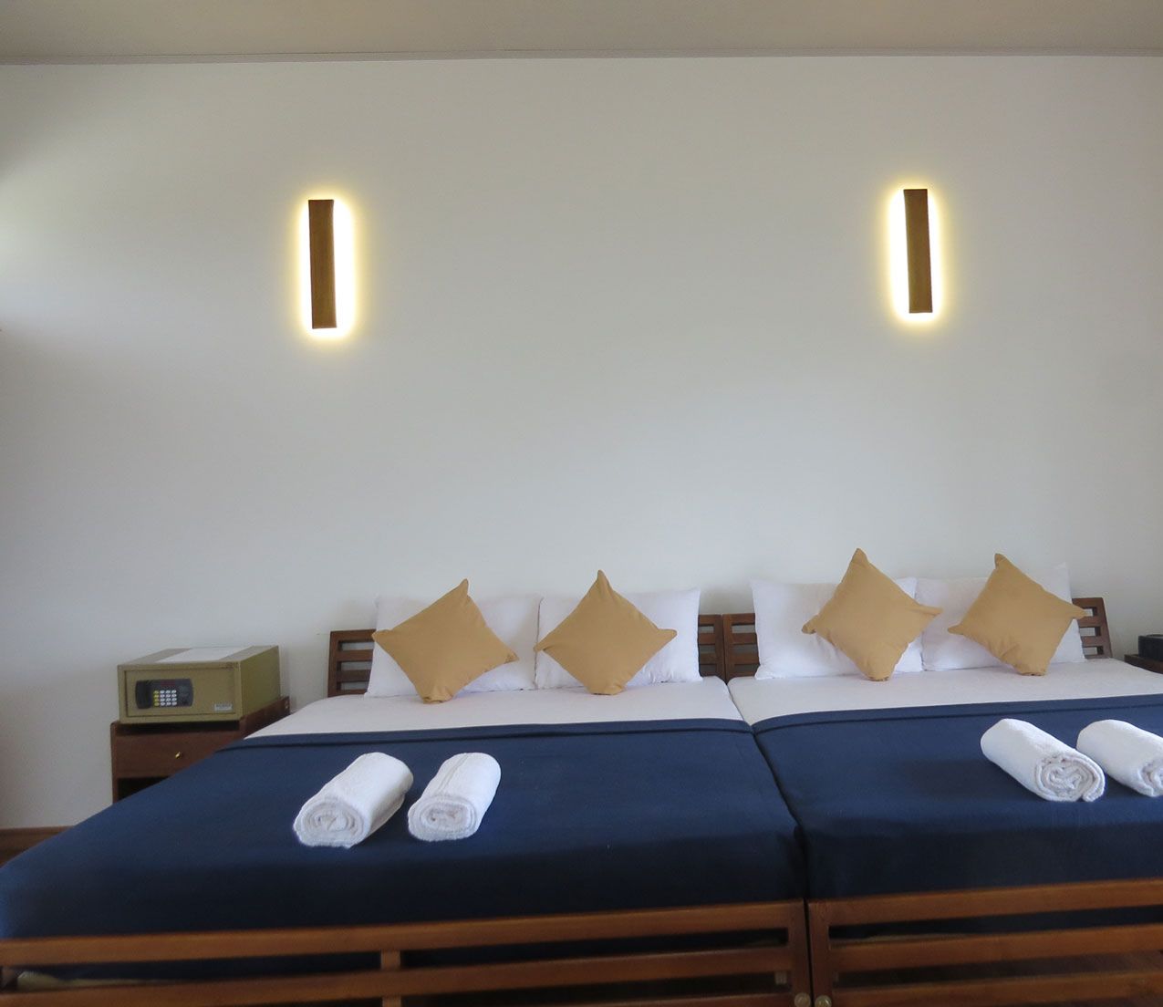 A double bed with two pillows, a bedside table, and two wall-mounted lights.