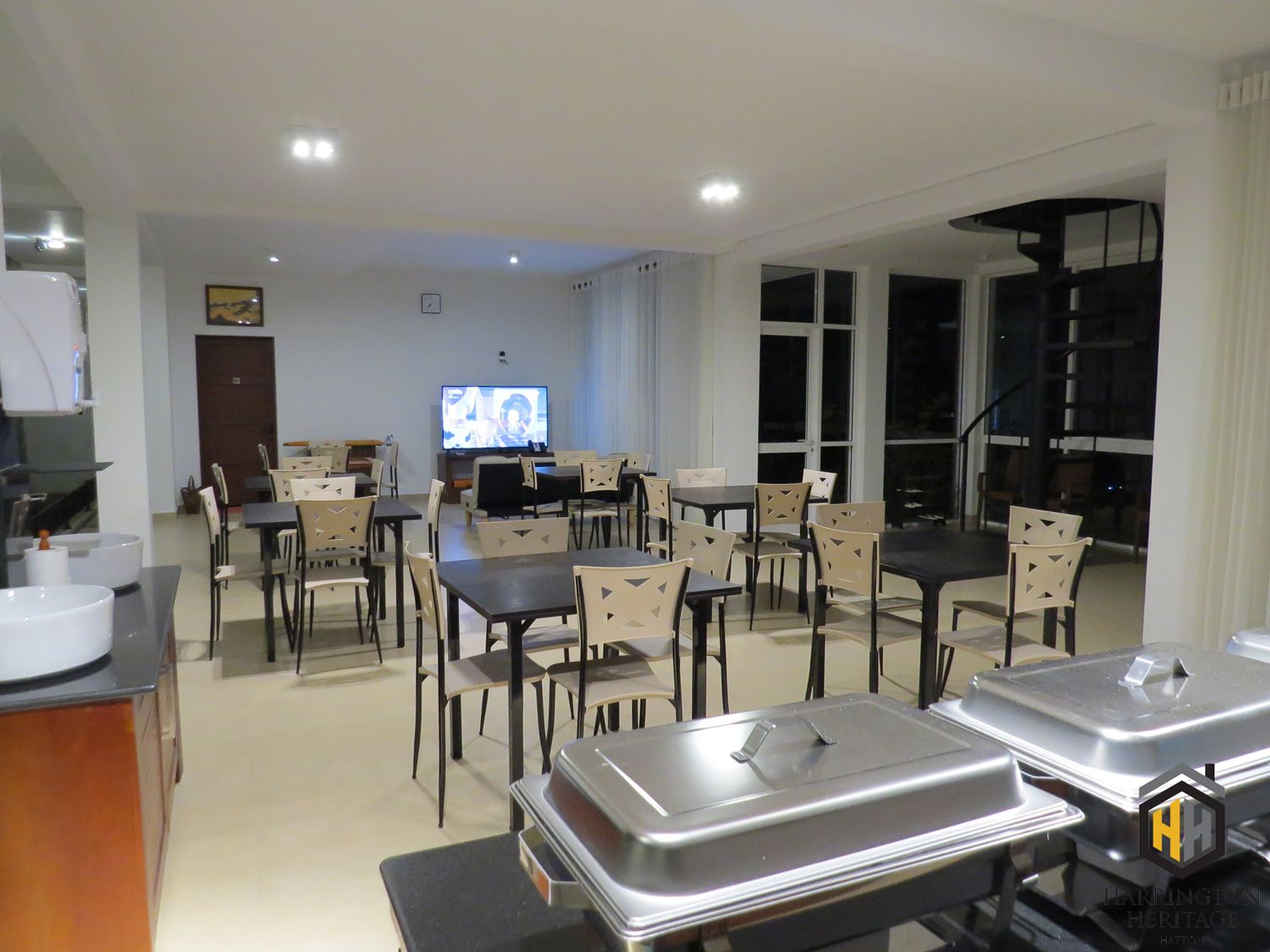 A hotel dining area with multiple tables and chairs, a television, and buffet trolleys.