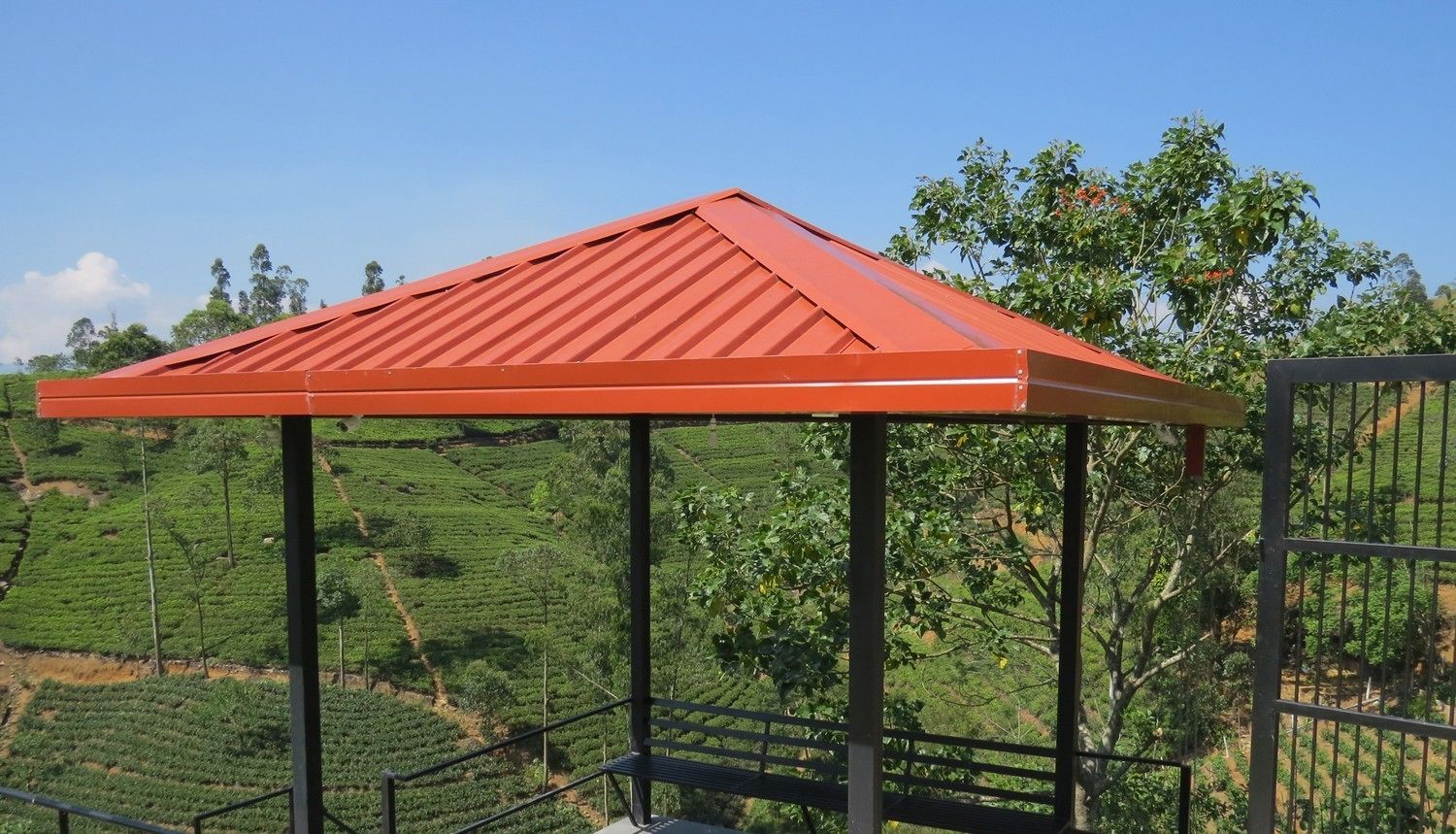 Une construction à toit rouge, dotée d’une structure métallique, qui surplombe une plantation de thé.