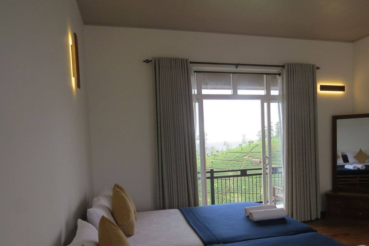 Habitación de hotel con una cama grande, un balcón con cortinas y vistas a un paisaje verde.
