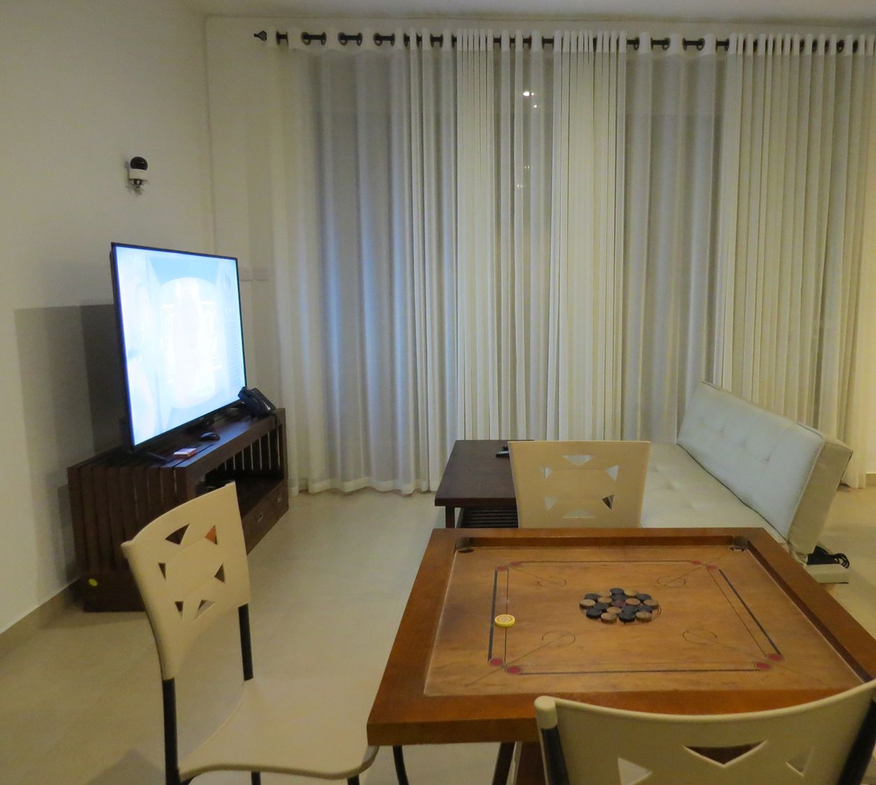 A living room with a television, a table with a board game, a sofa, and a chair.