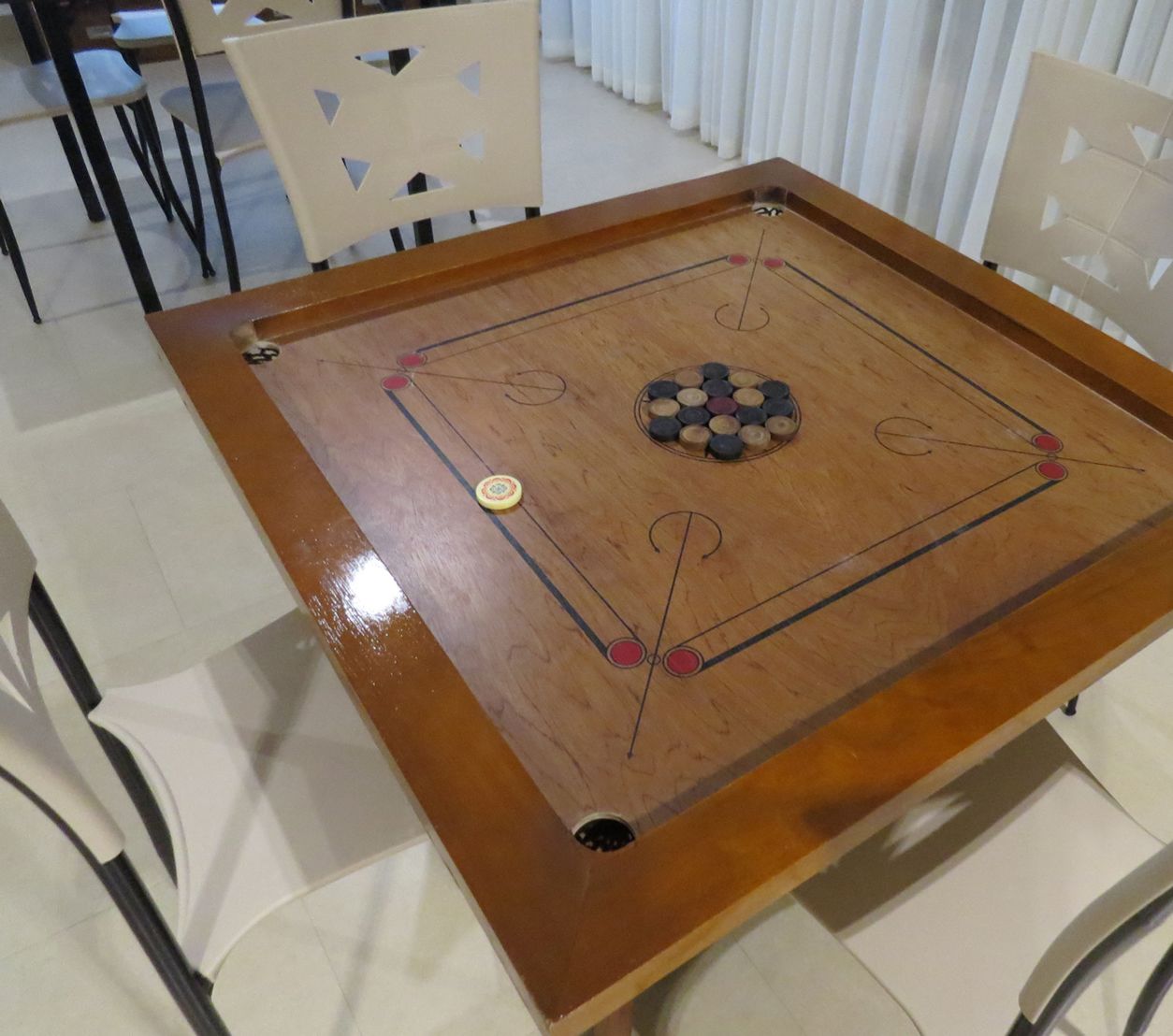 A wooden board game table with a central hole, surrounded by chairs.