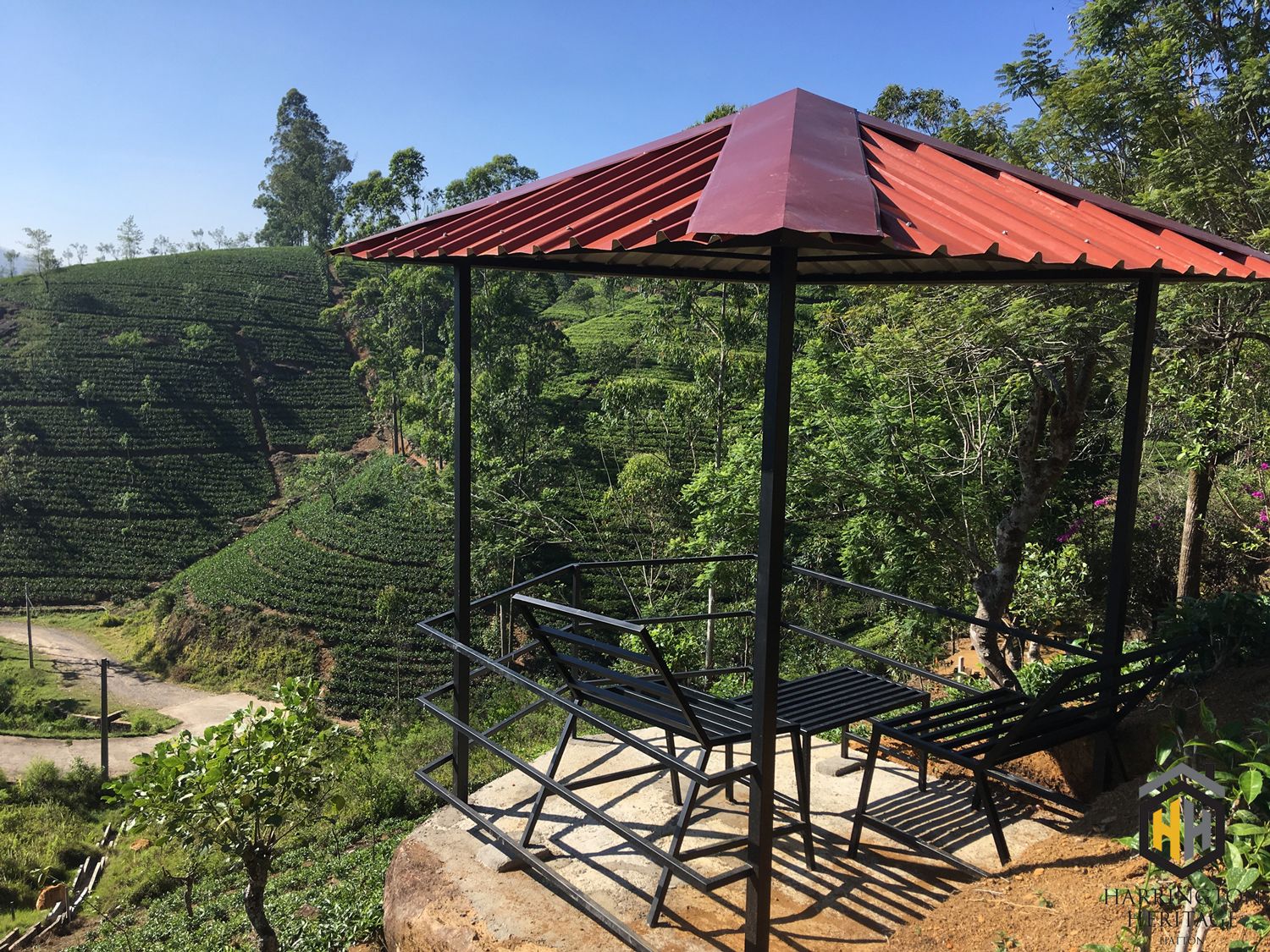 Ein Gazebo mit rotem Dach und Metallbänken, umgeben von üppigen, grünen Teeplantagen.