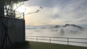 Uitzicht vanaf een balkon op een mistig landschap met bergen in de verte.