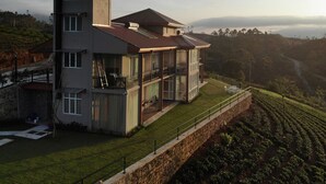 Een modern meerlaags huis met een balkon, grote ramen en uitzicht op een heuvelachtig landschap.