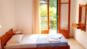 Un dormitorio con cama doble, cabecera de madera, mesita de noche, lámpara colgante, ventana con cortinas y vistas a zonas verdes.