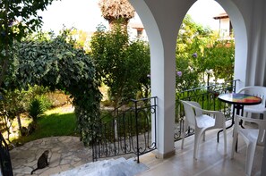 A covered outdoor area with a stone floor, white plastic chairs, and a table. - Villa Kostas (Corfu)