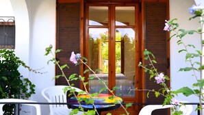Un balcón con puerta de madera, sillas blancas y una mesa de colores.