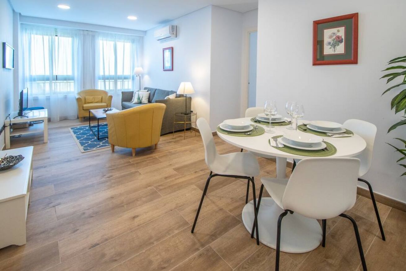 A modern living room with a dining area, featuring a round table set for four, a sofa, and a yellow armchair.
