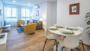 A modern living room with a dining area, featuring a round table set for four, a sofa, and a yellow armchair. - Apartamento Albatro´s suite (Cádiz)