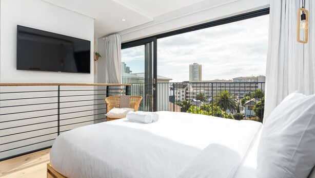 A modern hotel room with a large bed, a flat-screen TV mounted on the wall, and a balcony with a city view. - TenonQ C14 (Cape Town)