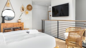 A modern bedroom with a bed, wooden dresser, wicker chair, and a TV mounted on the wall. - TenonQ C14 (Cape Town)