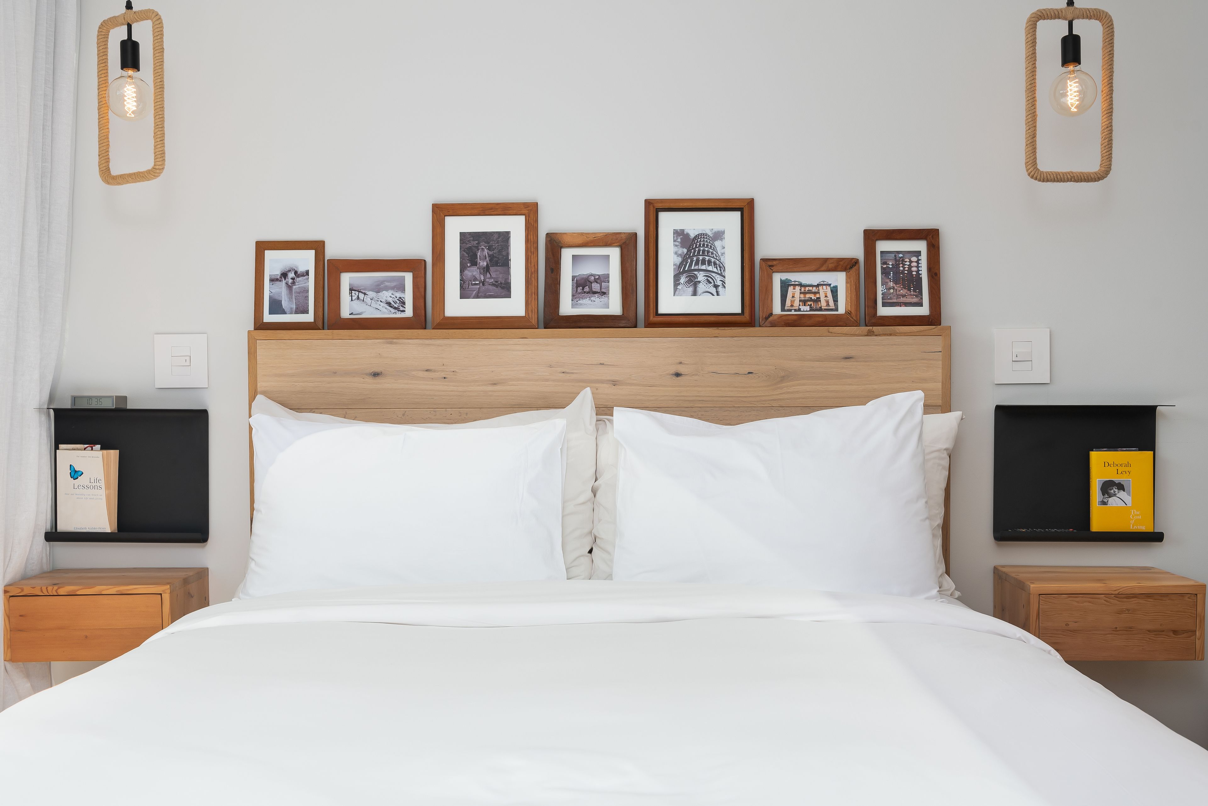 A neatly made bed with white linens, a wooden headboard, and a series of framed pictures on the wall above.