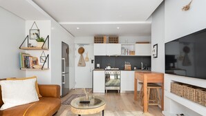 A modern living room with a sofa, coffee table, and kitchen area including a stove and cabinets. - TenonQ C14 (Cape Town)