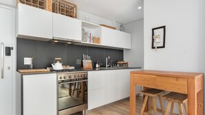 A modern kitchen with white cabinetry, a built-in oven, and a wooden dining table with two stools. - TenonQ C14 (Cape Town)
