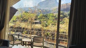 A balcony with chairs and a table, overlooking a rural landscape with vegetation and a distant mountain.