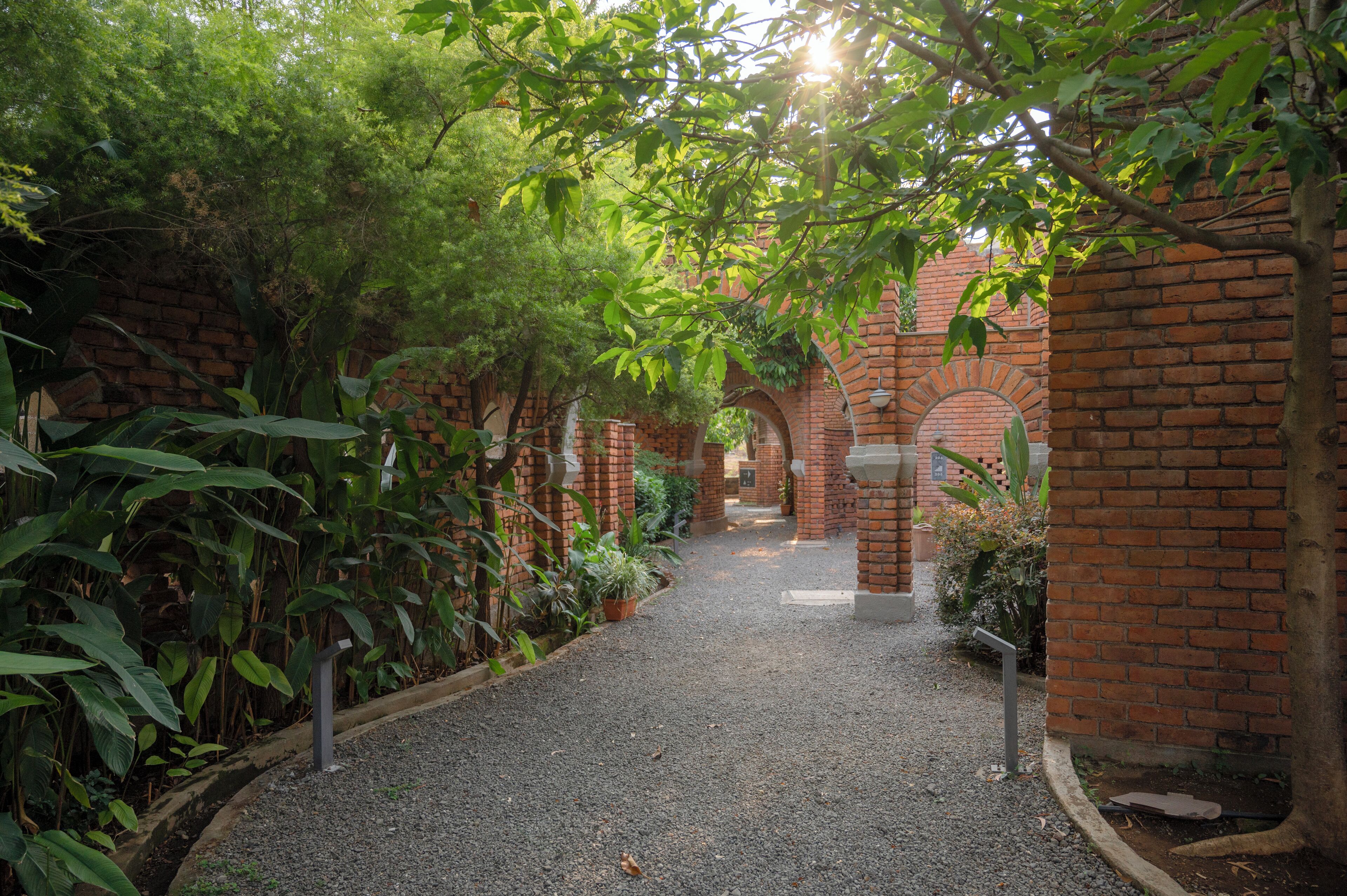 A pathway flanked by brick arches and lush greenery, leading to a brick building.