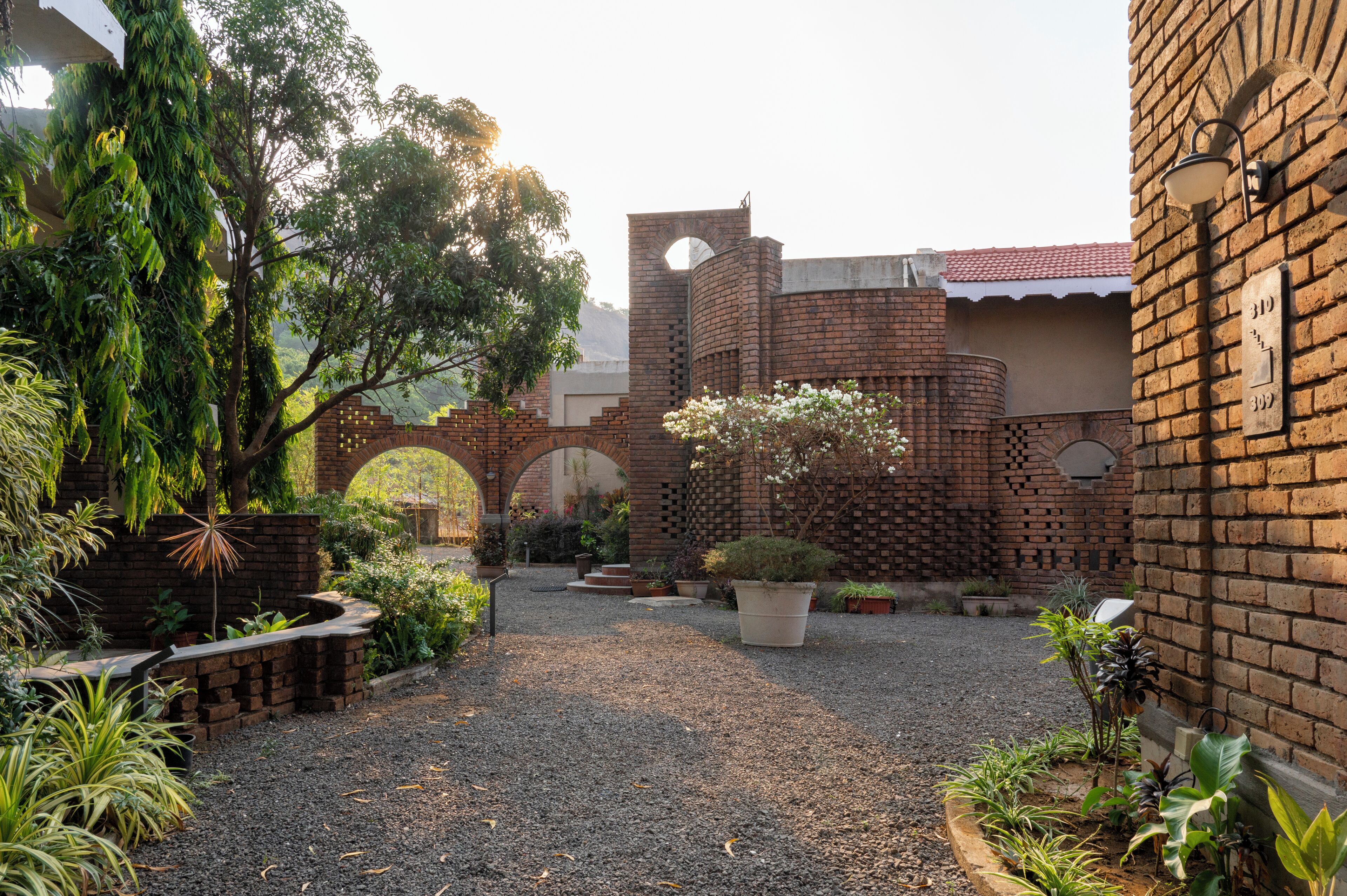A courtyard with brick walls, a central archway, and various potted plants.