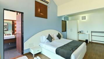 A modern hotel room with a large bed, bedside table, and a small desk with a chair. There is a wardrobe and a mirror on the wall.