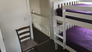 Une pièce avec des lits superposés, une chaise et une porte donnant sur une autre pièce.