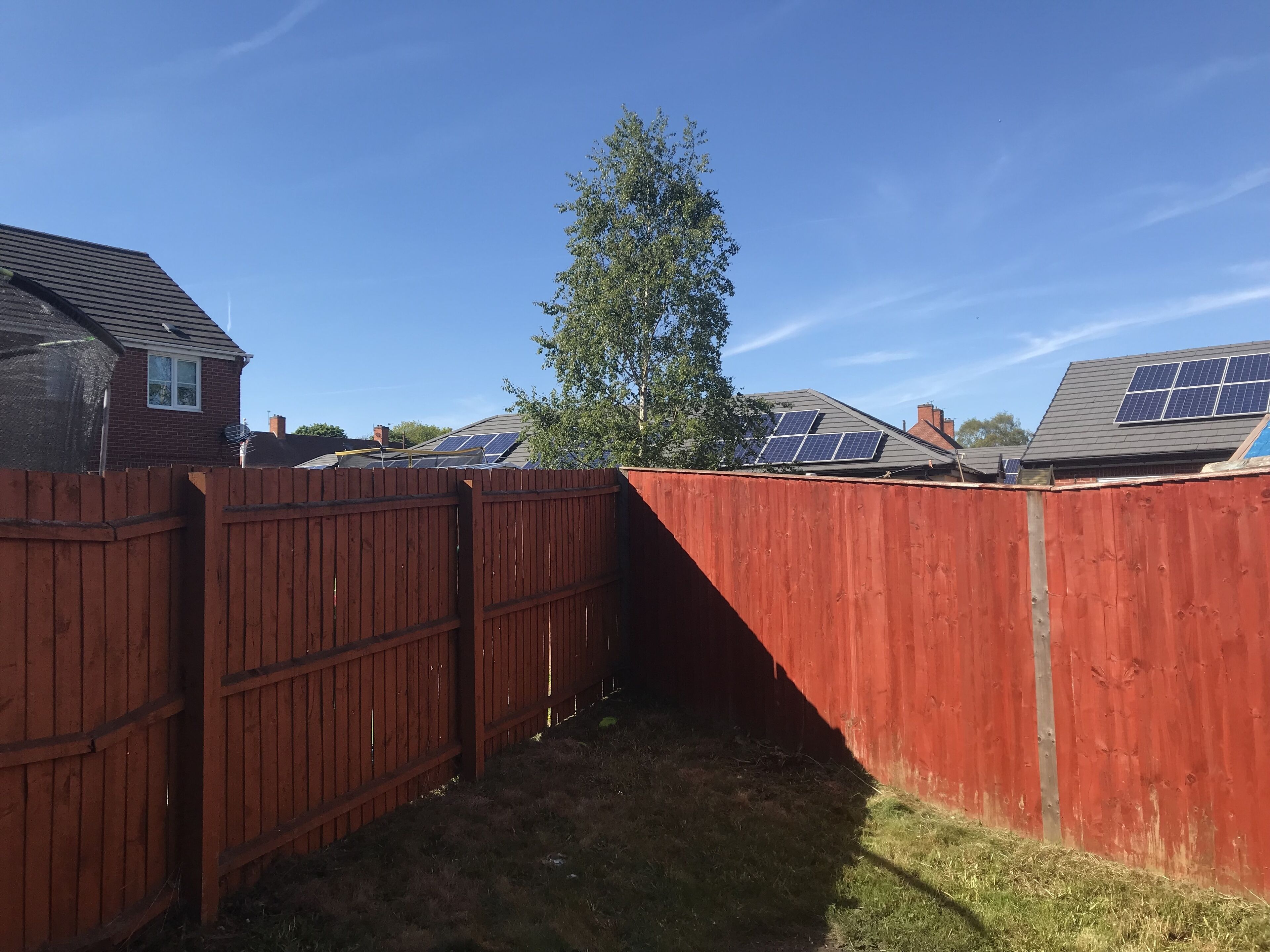 A fenced backyard with solar panels on the roof, a wooden fence, and a tree.