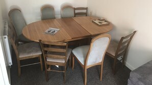 Une table de salle à manger ronde en bois, avec six chaises, un magazine posé sur la table et un petit objet décoratif.