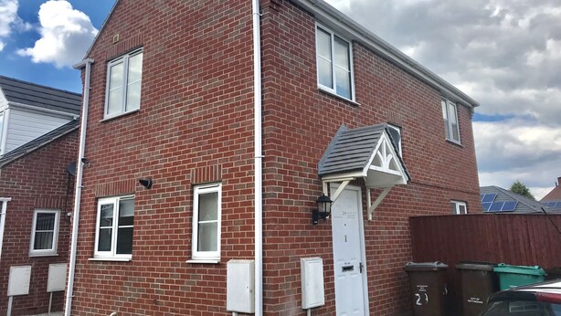 Une maison à deux étages, construite en briques, avec une porte blanche, des fenêtres et un petit garage attenant.