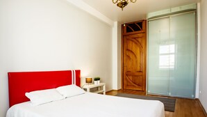 A bedroom with a red headboard, a white bedspread, a wooden door, and a sliding glass closet. - iRent.by Nemiga (Minsk)