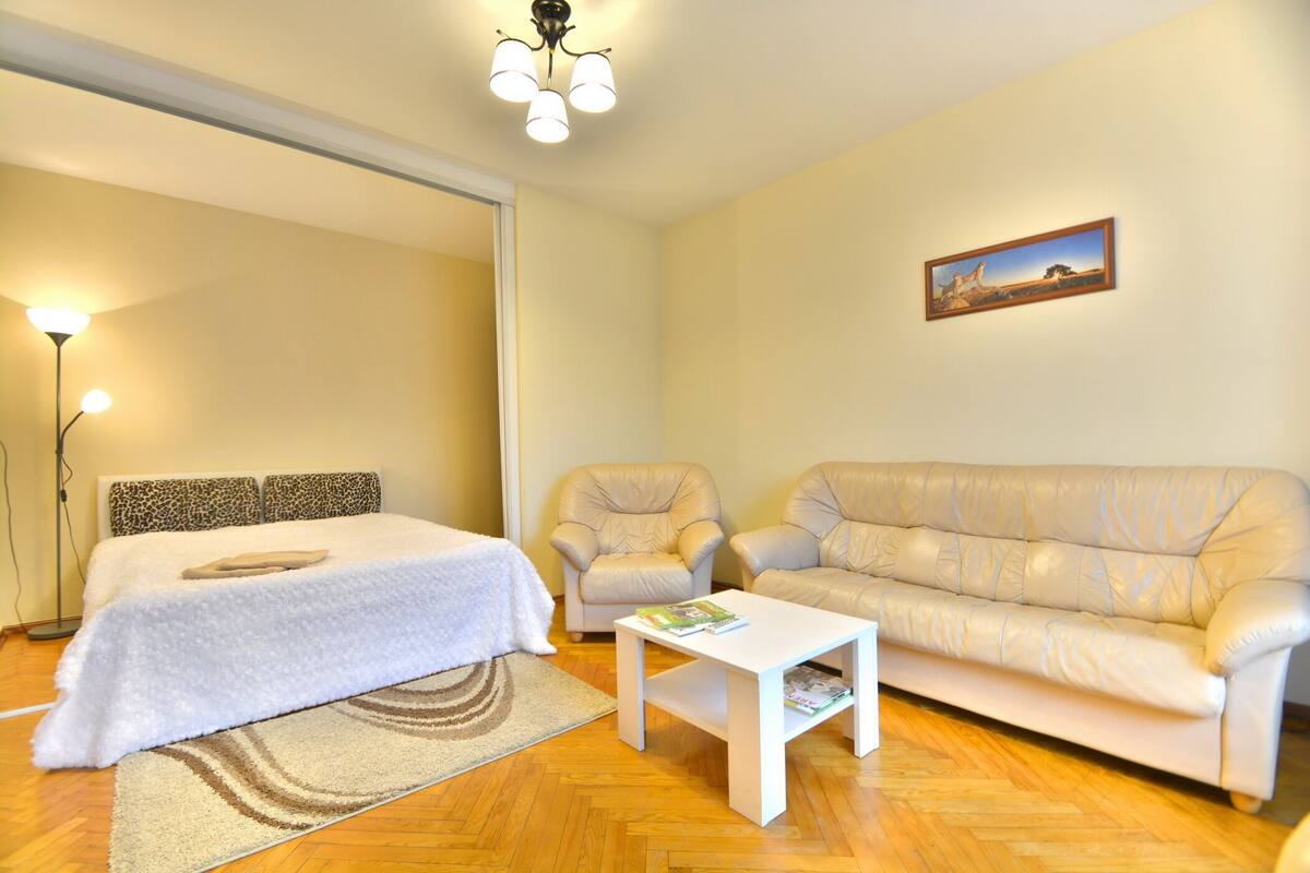 A bedroom with a bed, a sofa, a chair, a coffee table, and a painting on the wall.