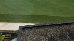 Un campo de golf con un club, una playa arenosa al fondo y cielo despejado.