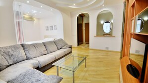 Ein modernes Wohnzimmer mit einem grauen Sofa, einem Glastisch, Holzböden und einem TV-Schrank aus Holz.