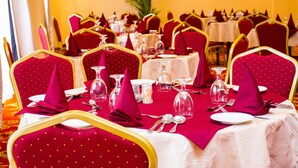 A banquet hall with tables set for dining, featuring red upholstered chairs with gold trim and white tablecloths. - Hotel Lakefield Exellence (Kandy)