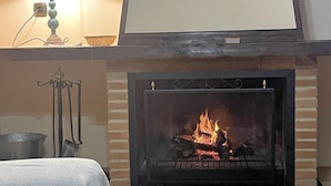 A fireplace with a visible fire, a metal pot, and a candle holder on a mantel. - Grazalema - La Tassone: Charming house, fireplace and terrace (Grazalema)