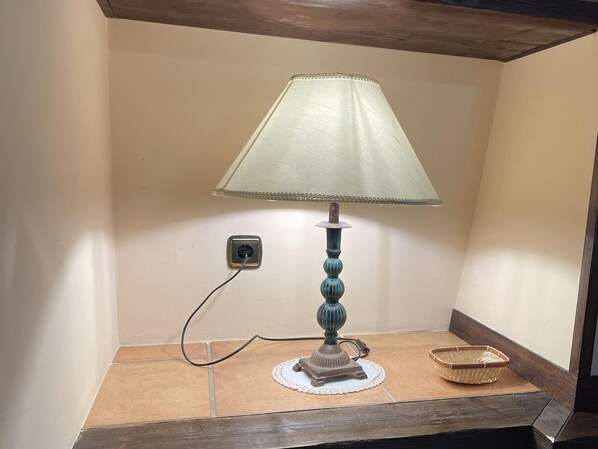 A table lamp with a white shade, connected to a power outlet on a tiled surface.