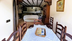 A dining area with a table set for two, wooden chairs, a chandelier, and a view into the kitchen. - Grazalema - La Tassone: Charming house, fireplace and terrace (Grazalema)