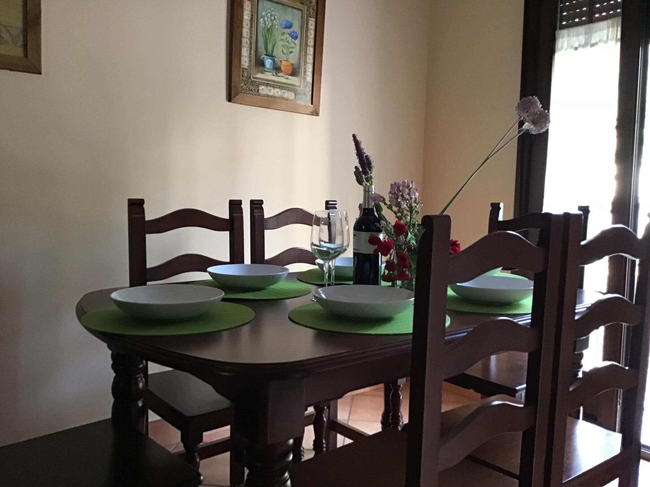 Een eettafel met groene tafelmatten, witte borden en een wijnfles.