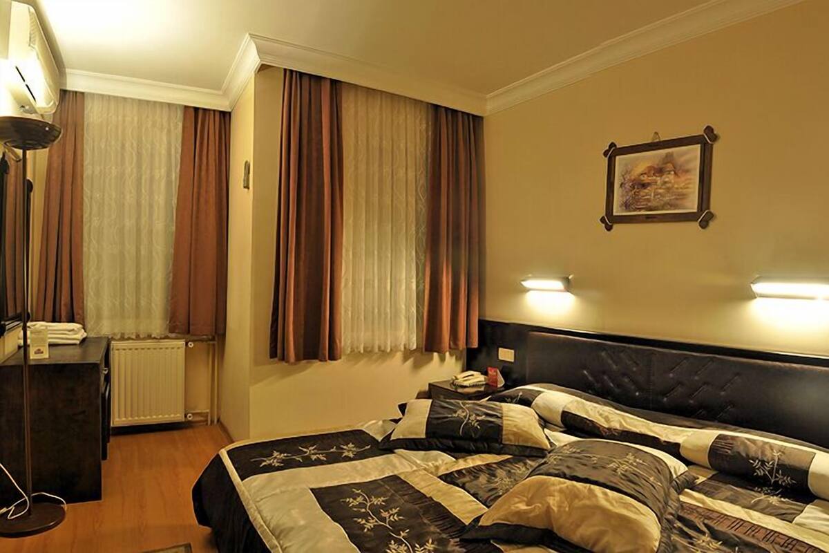 A hotel room with a bed, bedside lamps, a desk, and a radiator.