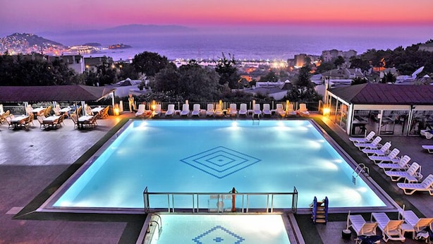 A large swimming pool with a geometric pattern, surrounded by sun loungers and a view of the sea at dusk. - Seaview Suite Hotel (Kusadasi)