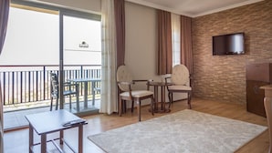 A hotel room with a balcony, a TV mounted on the wall, a small table with a chair, and a large rug on the floor. - Seaview Suite Hotel (Kusadasi)