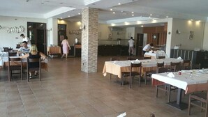 A spacious dining area with multiple tables and chairs, a central pillar, and a kitchen area in the background. - Seaview Suite Hotel (Kusadasi)