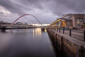 Une rivière traversée par un pont moderne, et un bâtiment situé au bord de l’eau, doté d’une façade en verre.