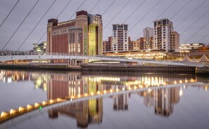Un paysage urbain au bord de l’eau, avec des bâtiments modernes, un pont et une rivière paisible qui reflète les lumières.