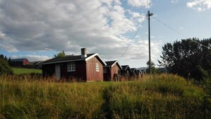 Ein ländliches Gehöft mit einem roten Holzhaus, umgeben von hohem Gras.