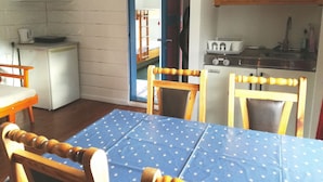 Eine kleine Küche mit Kühlschrank, Herd und Spüle. Ein Esstisch mit Stühlen und einer blauen Tischdecke steht bereit.