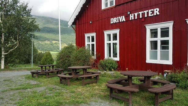 Ein rotes Gebäude namens 'DRIVA HYTTER' mit mehreren Picknicktischen außen.