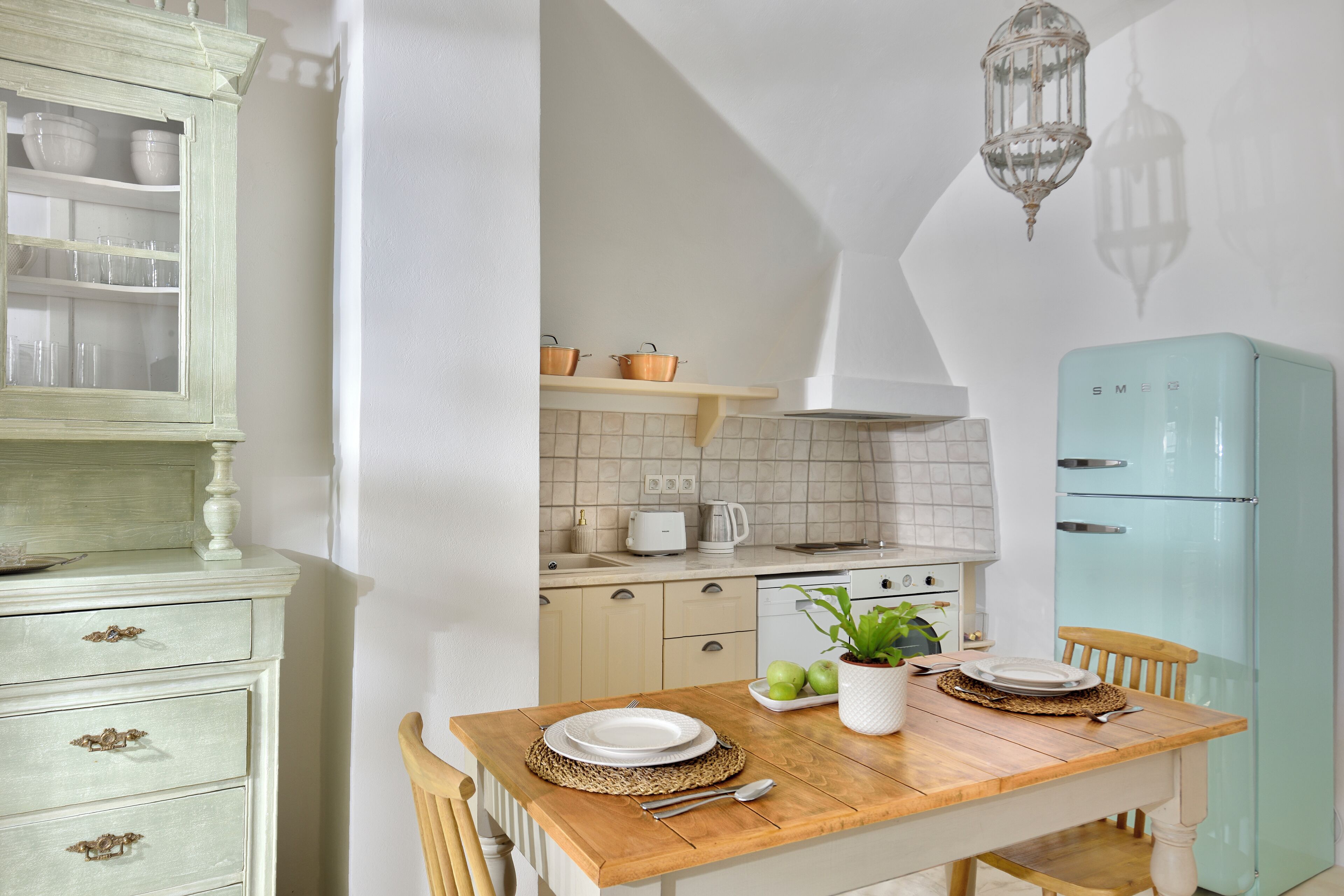 A kitchen with a wooden table set for dining, a light blue refrigerator, and a cabinet with glass doors.