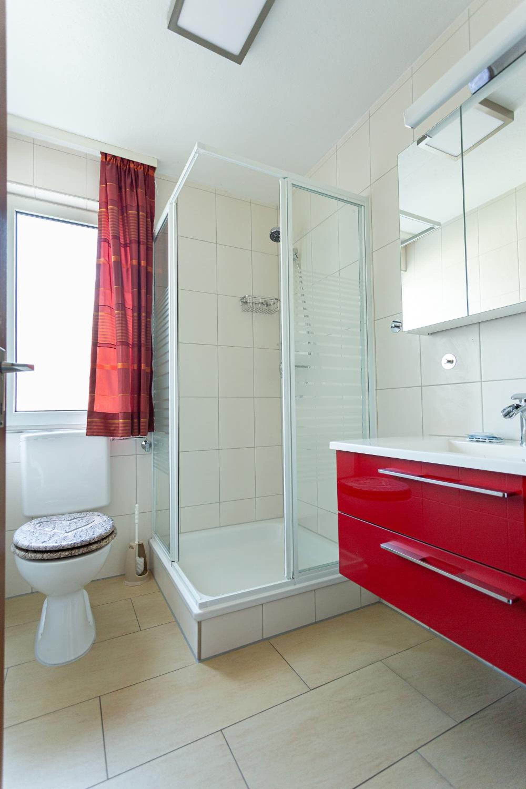 A bathroom with a glass shower enclosure, a toilet, and a red vanity with a mirror.