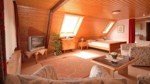 A cozy attic bedroom with a sloped ceiling, a bed, a TV, a small table, and a sofa. - Hotel Garni Silberdistel (Hinterzarten)